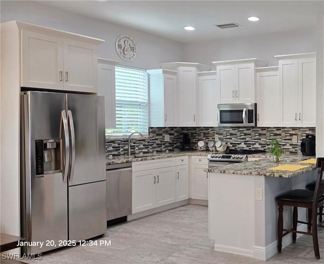 kitchen featuring kitchen peninsula, white cabinetry, a breakfast bar area, stainless steel appliances, and light stone counters