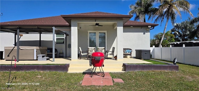 back of property featuring ceiling fan, a hot tub, a patio area, and a lawn