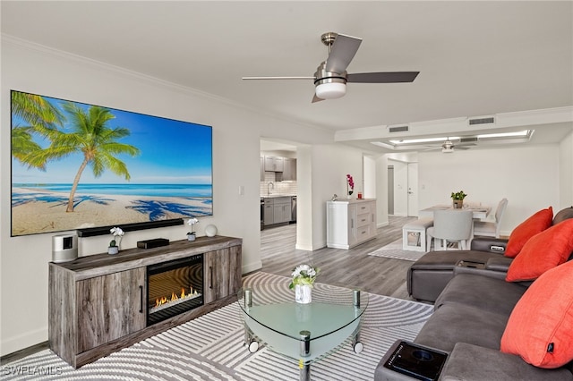 living room with hardwood / wood-style floors, crown molding, sink, and ceiling fan