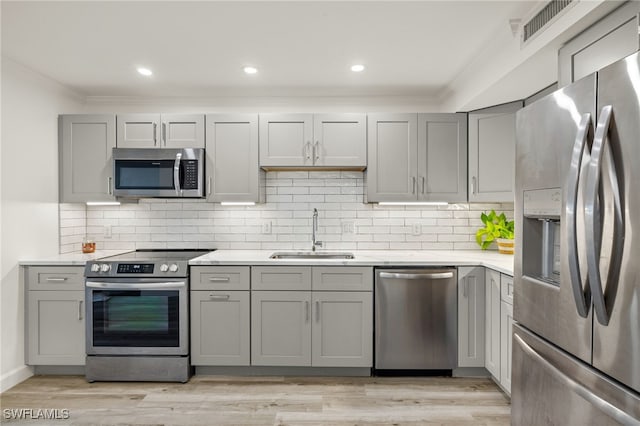 kitchen featuring sink, light hardwood / wood-style flooring, gray cabinets, stainless steel appliances, and decorative backsplash