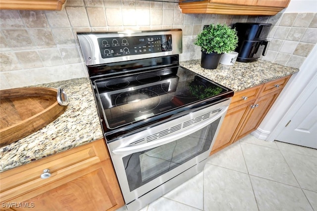 kitchen featuring light tile patterned floors, tasteful backsplash, stainless steel range with electric stovetop, and light stone countertops