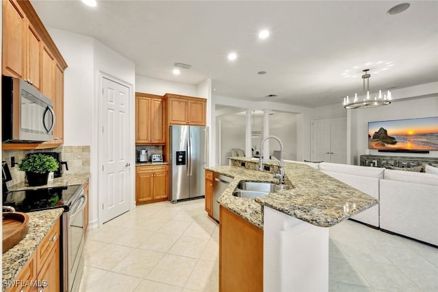 kitchen with stainless steel appliances, sink, backsplash, hanging light fixtures, and a center island with sink