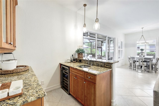 kitchen with wine cooler, hanging light fixtures, sink, plenty of natural light, and light stone counters