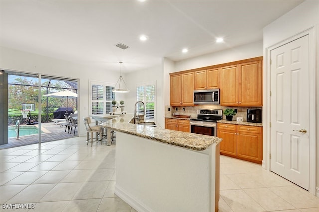 kitchen with light stone countertops, hanging light fixtures, light tile patterned floors, sink, and stainless steel appliances