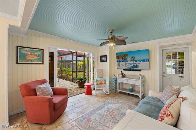 living room with ceiling fan, ornamental molding, and wooden walls