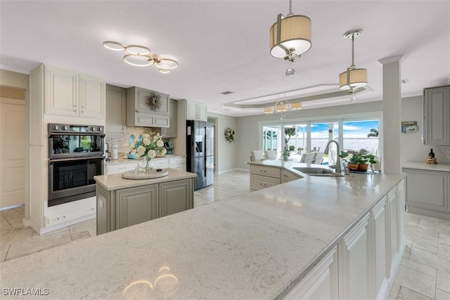 kitchen featuring stainless steel fridge with ice dispenser, multiple ovens, a large island, decorative light fixtures, and sink