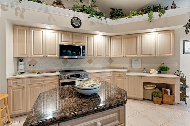 kitchen with light brown cabinets, appliances with stainless steel finishes, dark stone counters, light tile patterned floors, and decorative backsplash