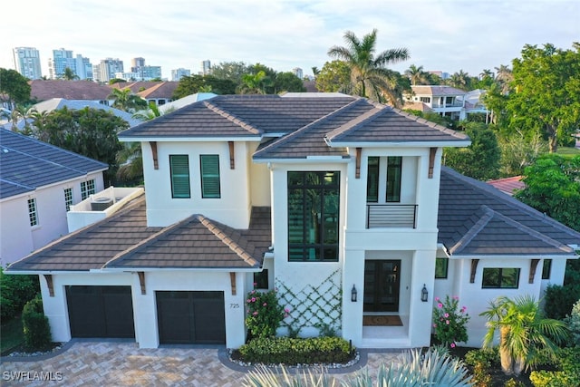 view of front facade with decorative driveway, a tiled roof, an attached garage, and stucco siding