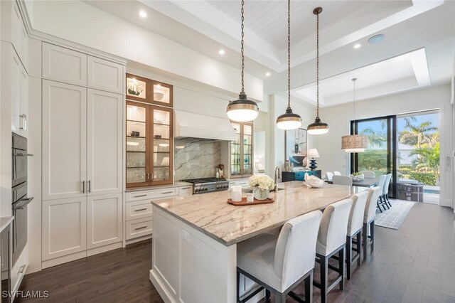 kitchen featuring white cabinetry, light stone counters, a center island, a raised ceiling, and decorative backsplash