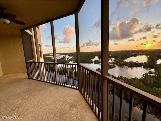 balcony at dusk featuring ceiling fan and a water view