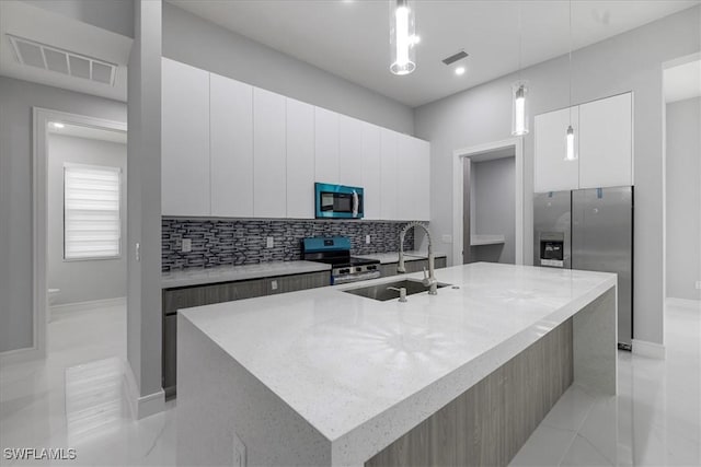 kitchen featuring an island with sink, stainless steel appliances, decorative light fixtures, white cabinets, and sink