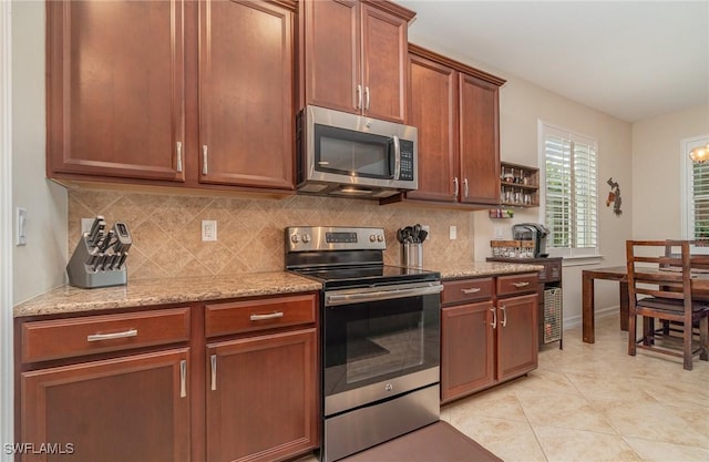 kitchen with decorative backsplash, light tile patterned flooring, light stone countertops, and appliances with stainless steel finishes