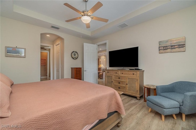 bedroom with light hardwood / wood-style flooring, a raised ceiling, and ceiling fan