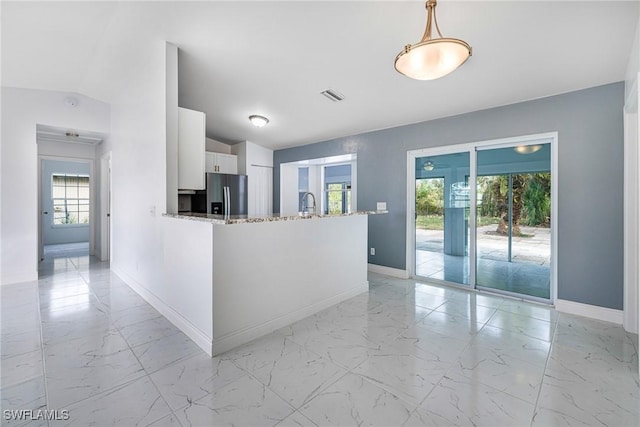 kitchen with white cabinetry, decorative light fixtures, stainless steel fridge, kitchen peninsula, and light stone countertops