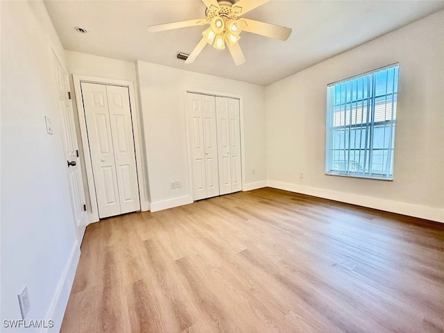 unfurnished bedroom featuring two closets, light hardwood / wood-style floors, and ceiling fan