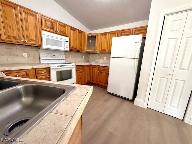 kitchen featuring sink, light wood-type flooring, white appliances, decorative backsplash, and lofted ceiling