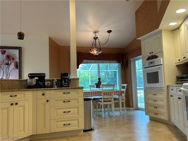 kitchen with decorative light fixtures, dark stone countertops, light tile patterned floors, and white oven