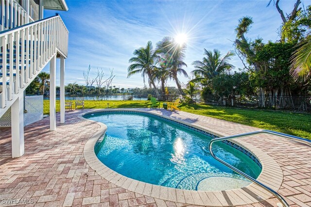 view of pool featuring a lawn, a water view, and a patio