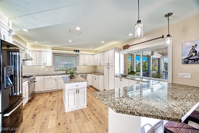 3131 Twin Lakes Ln, Sanibel, FL 33957 - kitchen with black fridge with ice dispenser, stainless steel stove, light wood-style floors, under cabinet range hood, and white cabinetry