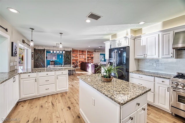 kitchen with stainless steel range with gas stovetop, decorative light fixtures, white cabinets, a barn door, and black fridge