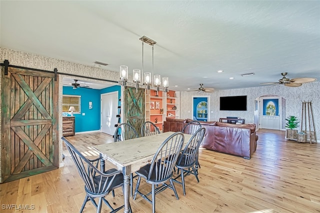 dining room with ceiling fan, a barn door, and light wood-type flooring