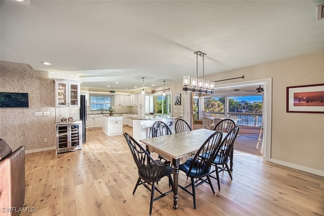 dining area featuring light hardwood / wood-style floors, a chandelier, wine cooler, and a healthy amount of sunlight