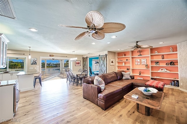 living room with ceiling fan, a textured ceiling, a barn door, and light wood-type flooring