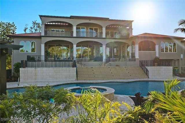 rear view of house with a balcony and a pool with hot tub