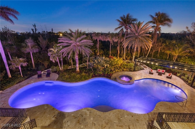 pool at dusk with a patio and an in ground hot tub