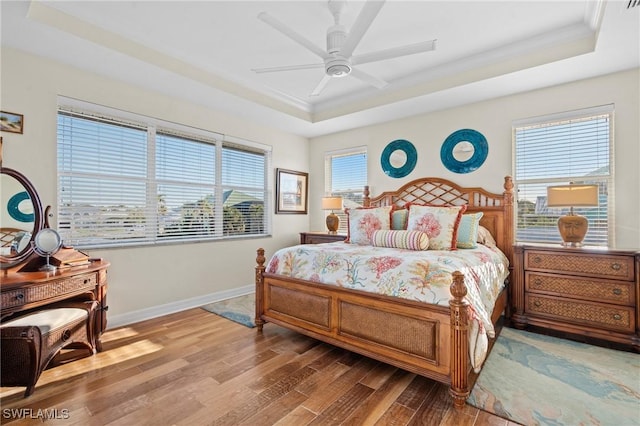 bedroom with a raised ceiling, multiple windows, baseboards, and wood finished floors