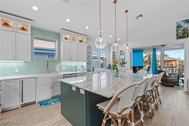 kitchen featuring glass insert cabinets, white cabinetry, a center island with sink, and hanging light fixtures