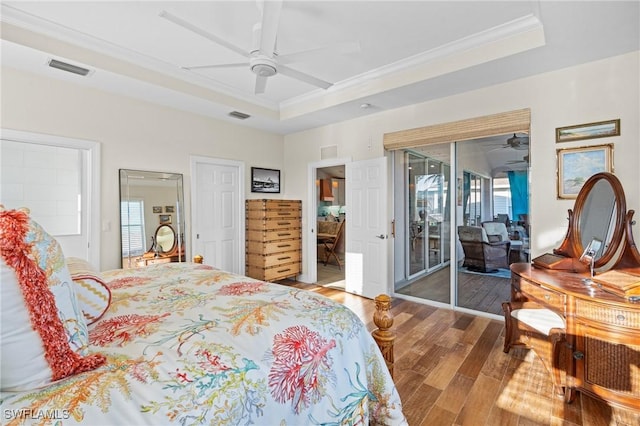 bedroom with access to exterior, a tray ceiling, crown molding, visible vents, and wood finished floors