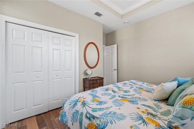 bedroom featuring dark wood finished floors, visible vents, ornamental molding, a closet, and a raised ceiling