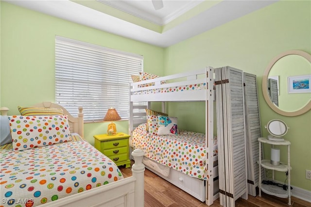 bedroom featuring crown molding, a raised ceiling, a ceiling fan, wood finished floors, and baseboards