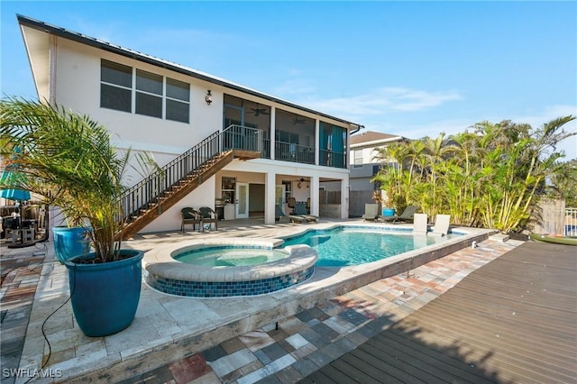 rear view of property with a sunroom, a patio area, stairs, and a pool with connected hot tub