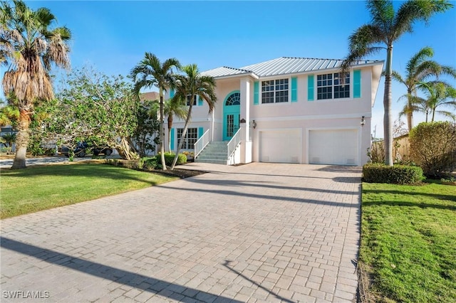 view of front of house with decorative driveway, stucco siding, an attached garage, a front yard, and metal roof