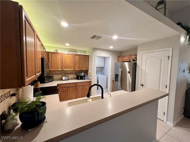 kitchen with washer / dryer, light tile patterned floors, kitchen peninsula, stainless steel appliances, and sink