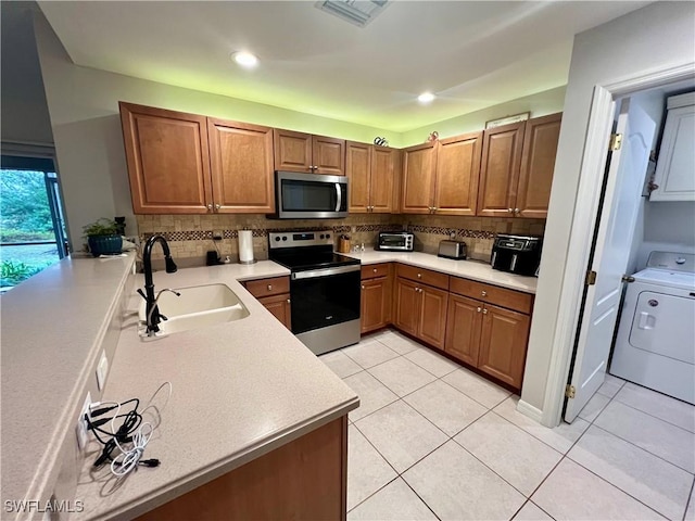 kitchen featuring appliances with stainless steel finishes, sink, washer / dryer, and light tile patterned flooring