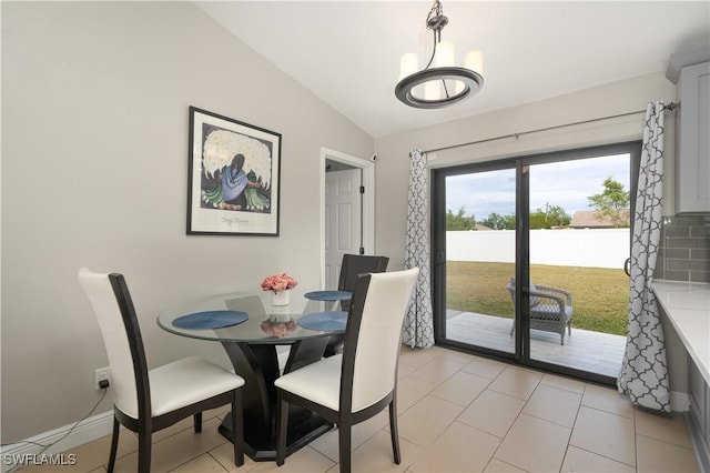 tiled dining space featuring a notable chandelier and vaulted ceiling