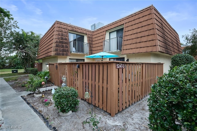 view of side of property with stucco siding, a fenced front yard, mansard roof, and a balcony