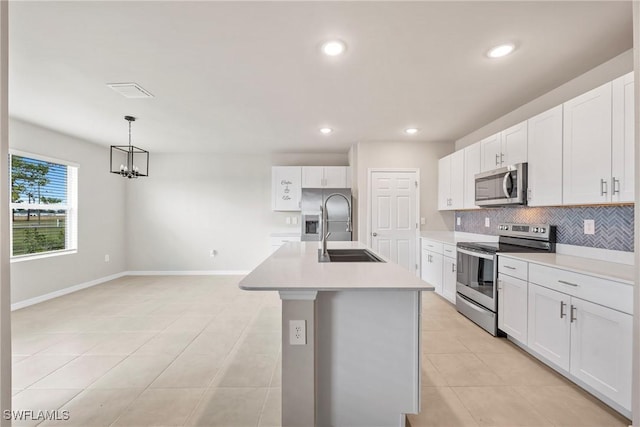 kitchen with appliances with stainless steel finishes, white cabinets, decorative light fixtures, sink, and an island with sink