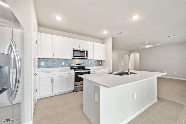 kitchen with appliances with stainless steel finishes, sink, white cabinets, light tile patterned flooring, and a kitchen island with sink