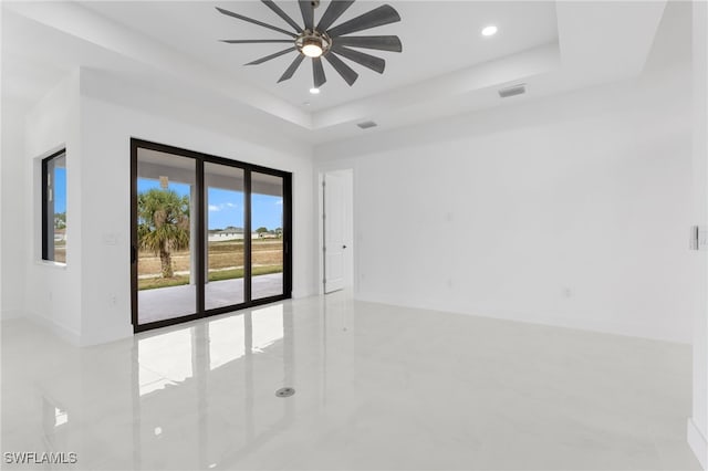 empty room with ceiling fan, a wealth of natural light, and a raised ceiling