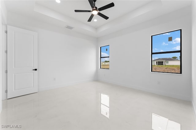 spare room featuring ceiling fan, a wealth of natural light, and a tray ceiling