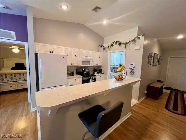 kitchen featuring white appliances, white cabinets, lofted ceiling, and a breakfast bar area