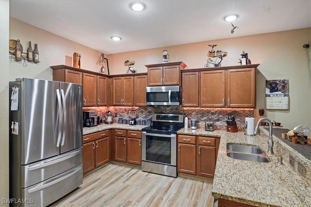 kitchen featuring appliances with stainless steel finishes, decorative backsplash, sink, light wood-type flooring, and light stone counters