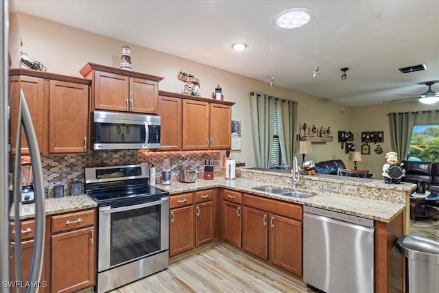 kitchen featuring sink, light wood-type flooring, kitchen peninsula, backsplash, and stainless steel appliances