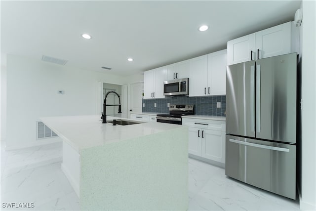 kitchen with stainless steel appliances, sink, white cabinetry, and a kitchen island with sink