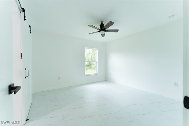 empty room featuring ceiling fan and a barn door