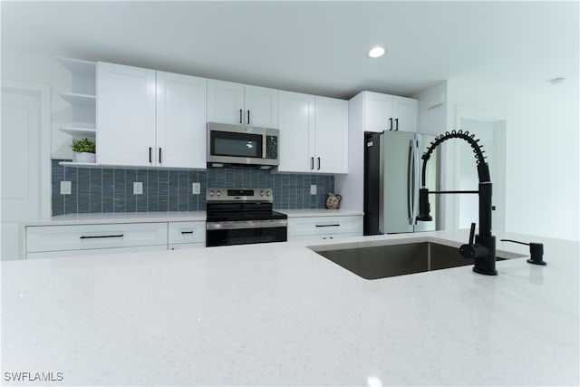 kitchen with white cabinetry, stainless steel appliances, backsplash, light stone countertops, and sink